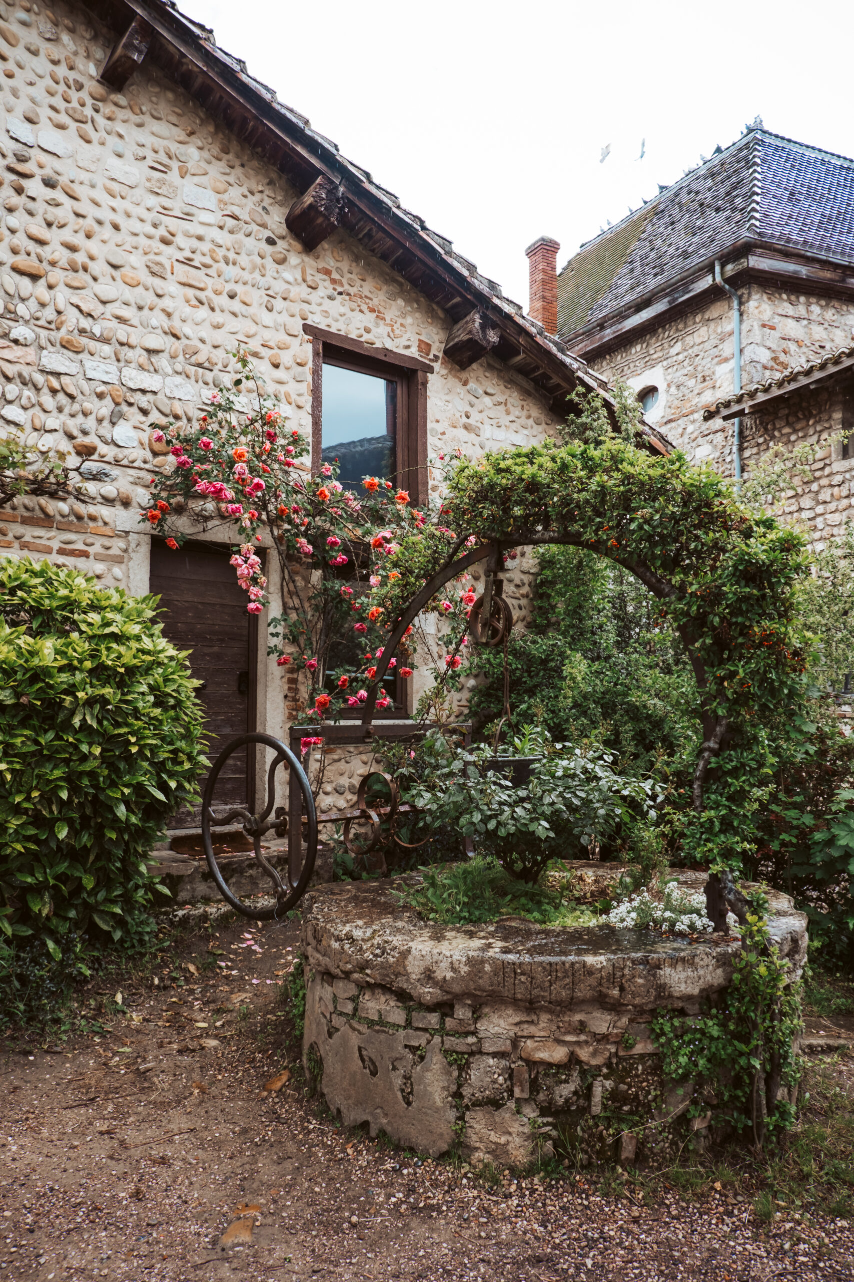 cobble stone street with lush roses and greenery surrounding a stone well. A beautiful place to get married in France.